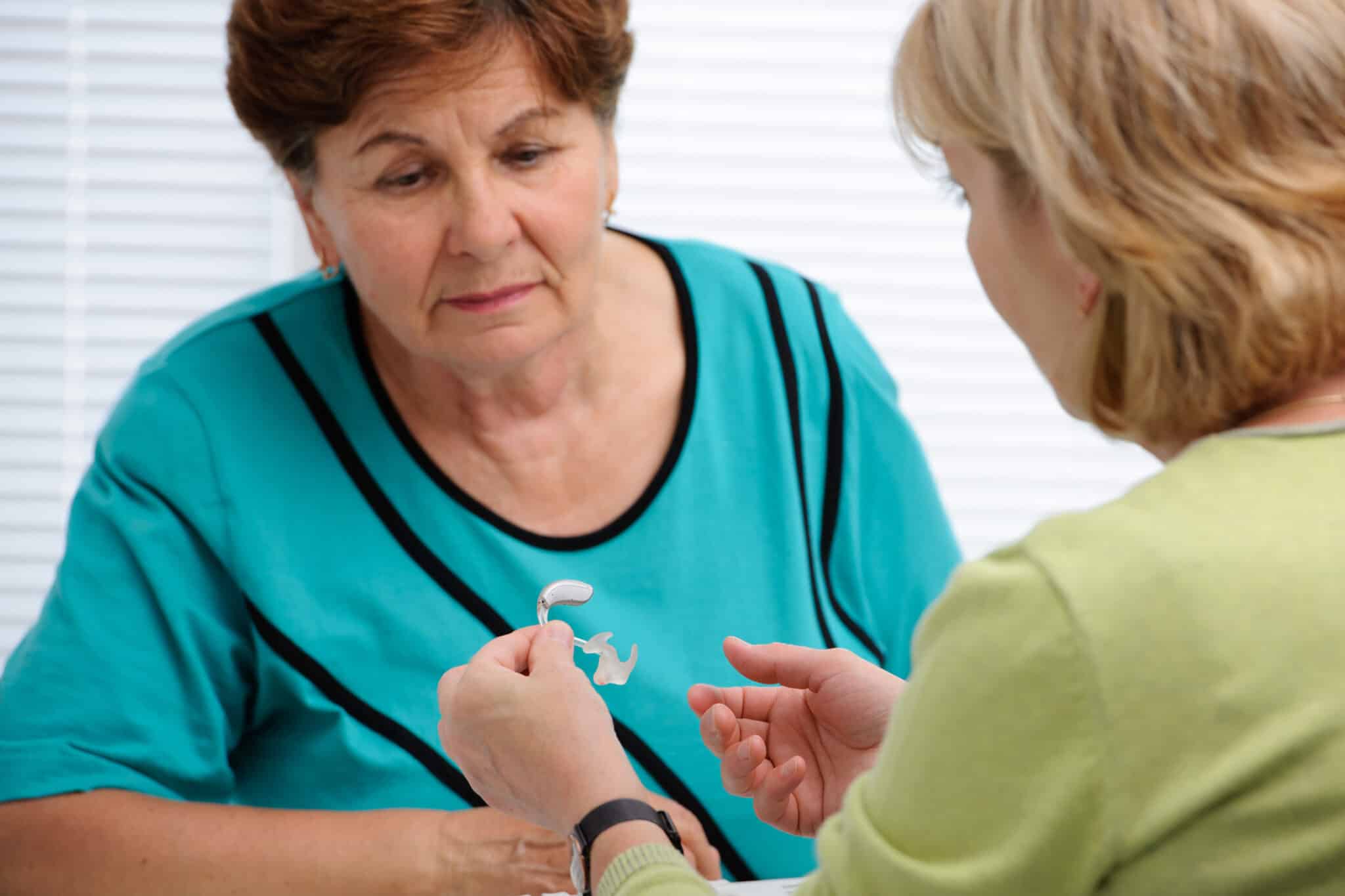 Audiologist showing a patient how to use hearing aids.