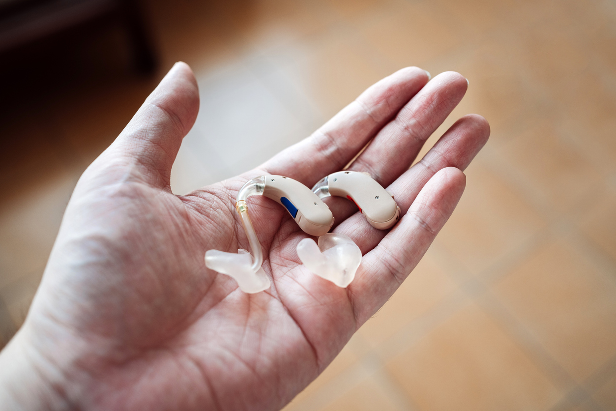 A hand holding a pair of modern hearing aids with custom ear molds